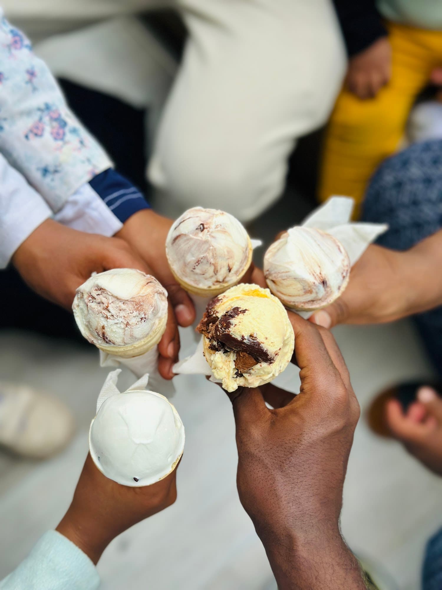 Close-up of four people holding their gelato cones together in a celebratory toast